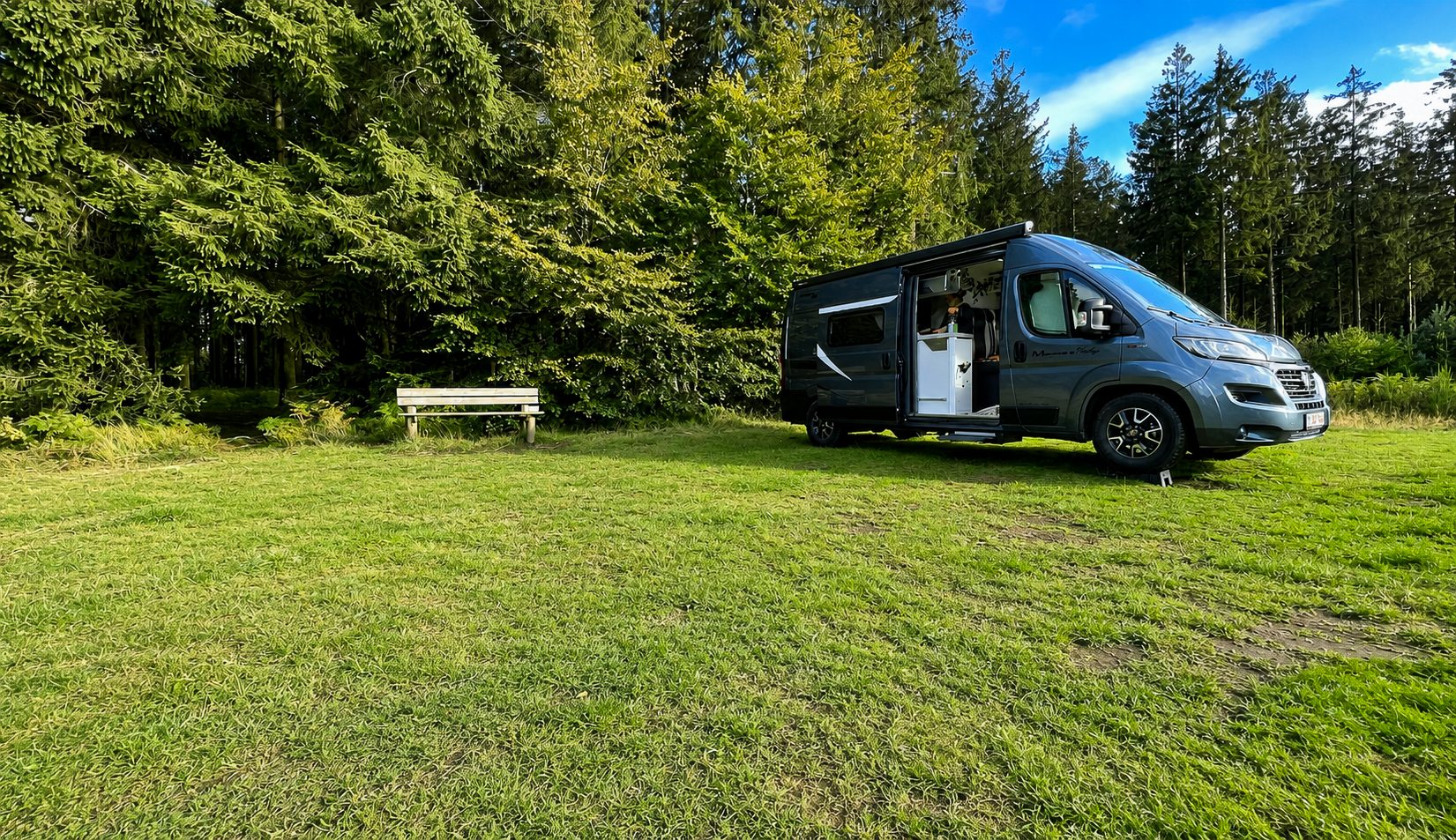 Camper Freddy op een groene kampeerplaats aan de bosrand